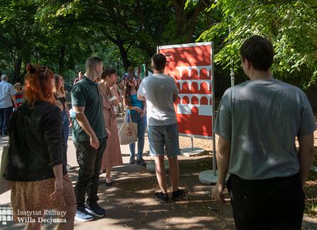 fotografia. wystawa Wyszehrad to ludzie na krakowskich plantach. ludzie przechadzają się pomiędzy plakatami ustawionymi w rzędzie wzdłuż alejki.